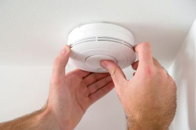 Close-up of a person pressing a button on a smoke alarm to check that it works.